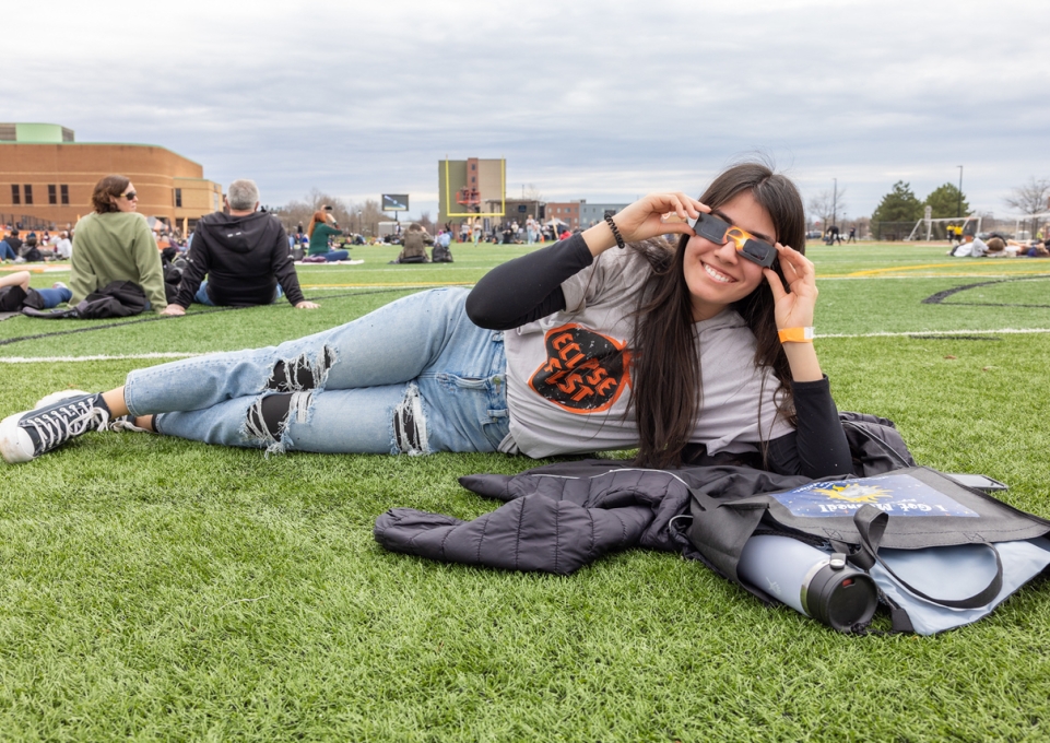 Girl with eclipse glasses on field